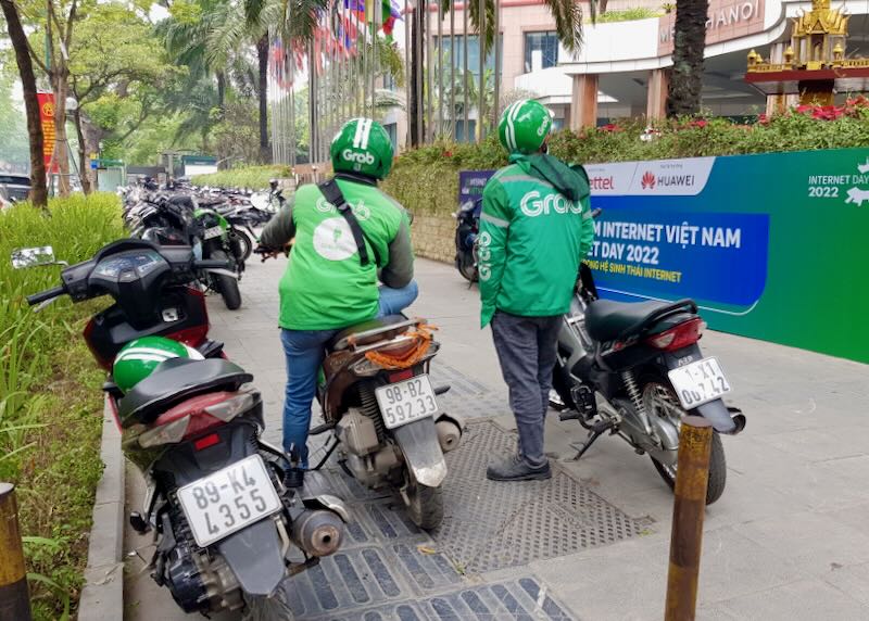 Two people dressed in green "Grab" jackets sit on motorcycles, waiting for customers.