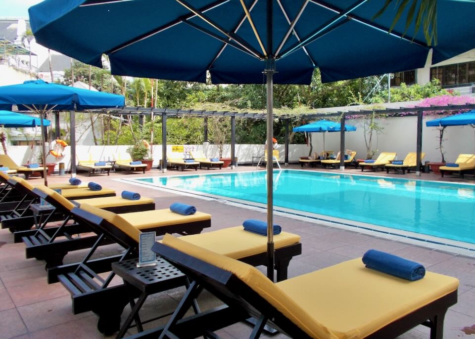 Yellow cushioned lounge chairs surround a aqua blue rectangular pool.