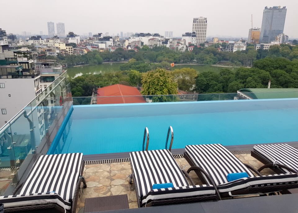 Black and white striped lounge chairs sit next to a pool overlooking the city from the roof.