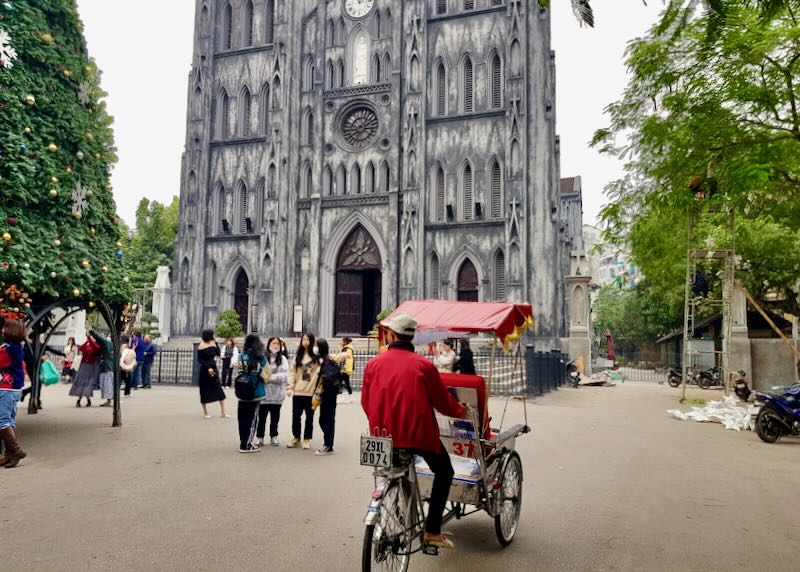 A man on a rickshaw rides in front of St. Joseph’s Cathedral.