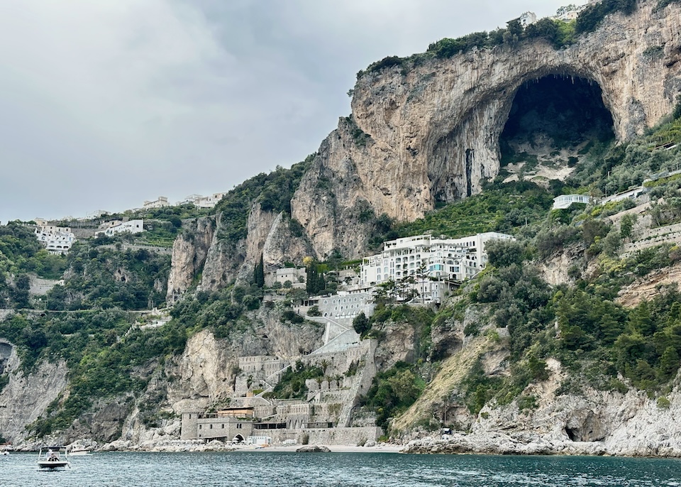 Borgo Santandrea hotel under a giant cave with a white exterior that gradually turns into a stone fortress as it meets the sea in Amalfi