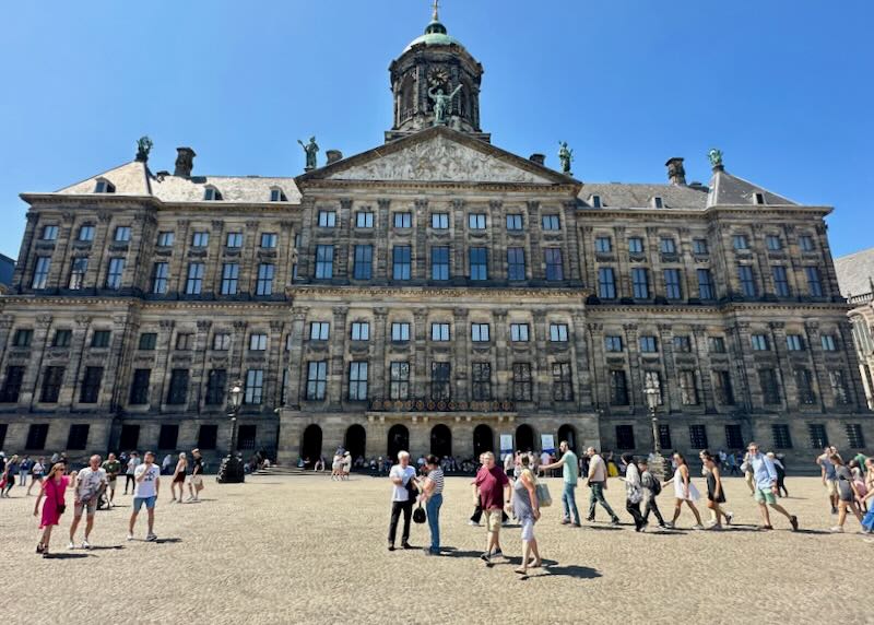 People walk in the pedestrian plaza outside the Amsterdam Royal Palace on a sunny day