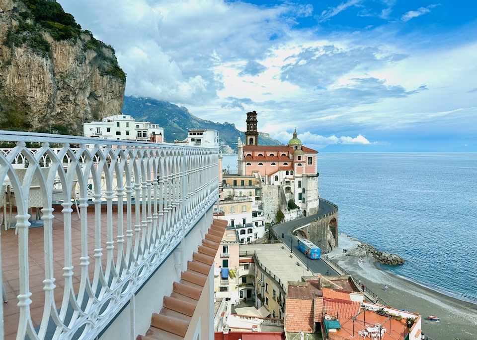 The sun terrace with white railings and terracotta flooring overlooking the sea and domed church at Palazzo Ferraioli hotel in Atrani