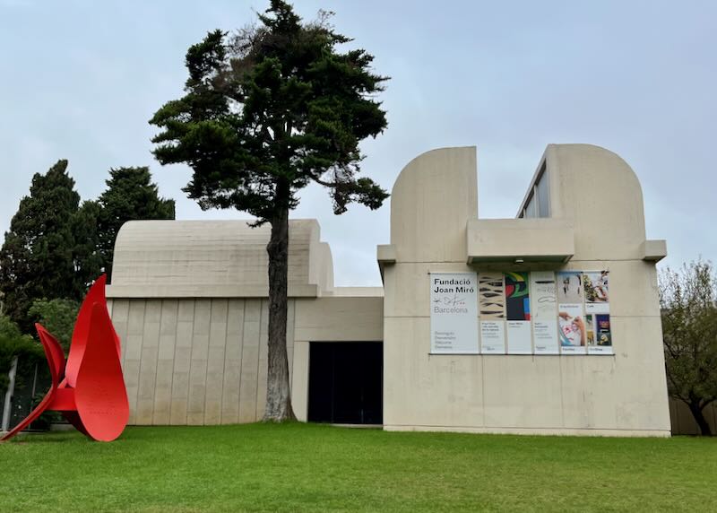 Modernist concrete building with red modern sculpture in front.