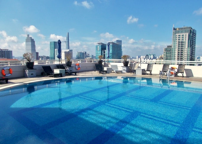 A rooftop blue pool with lounge chairs overlooks the city.