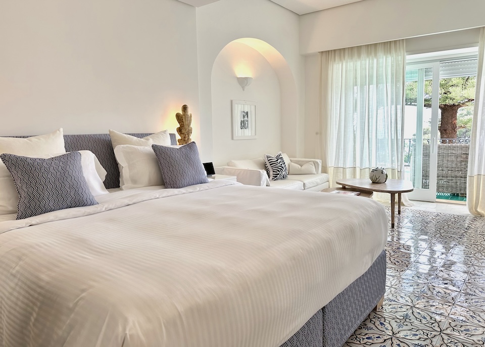 A plush king-sized bed and sofa with maiolica tile floors in white and blue in a superior room at La Minerva hotel in Capri