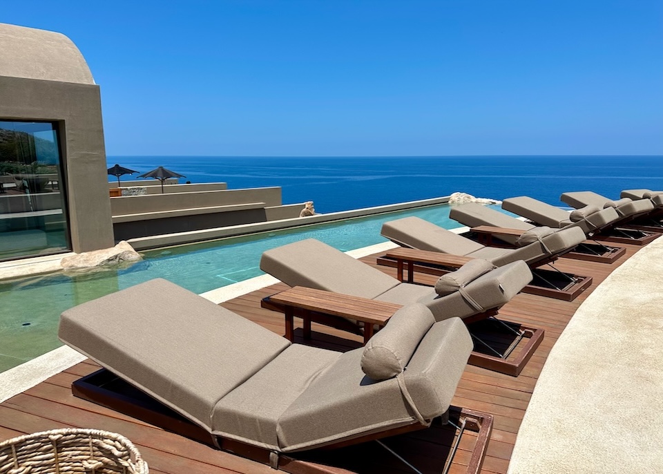 Sunbeds with elevated feet along a curved infinity pool above the sea at Acro Wellness Suites in Crete