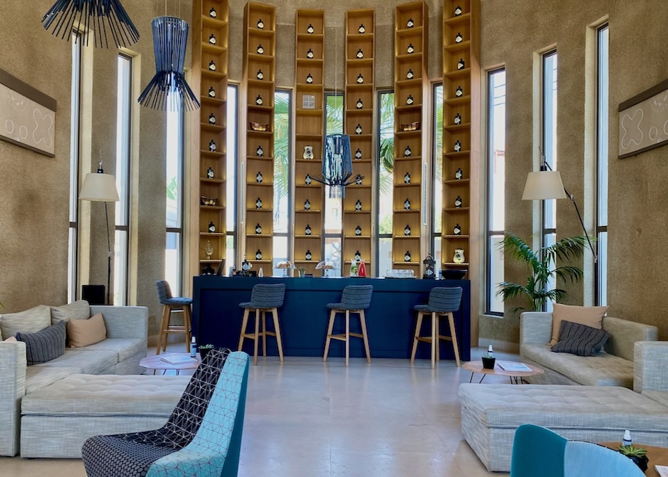 Lobby bar in blue, gold, and taupe with a high ceiling and skinny vertical windows interspersed with tall shelves at Domes Noruz resort in Crete