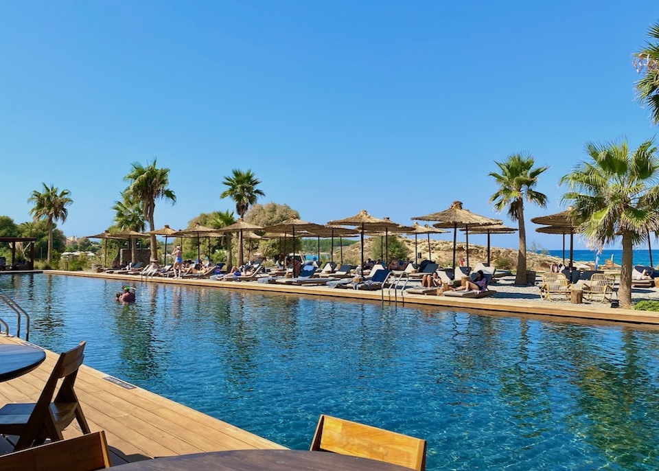 Beachfront pool with sunbeds and umbrellas and a glimpse of the sea at Domes Zeen resort in Crete