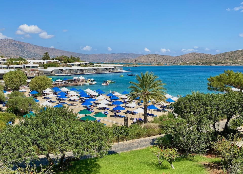 Overlooking the blue and white umbrellas on the beach with a private pier jutting into the sea at Elounda Beach Resort in Crete