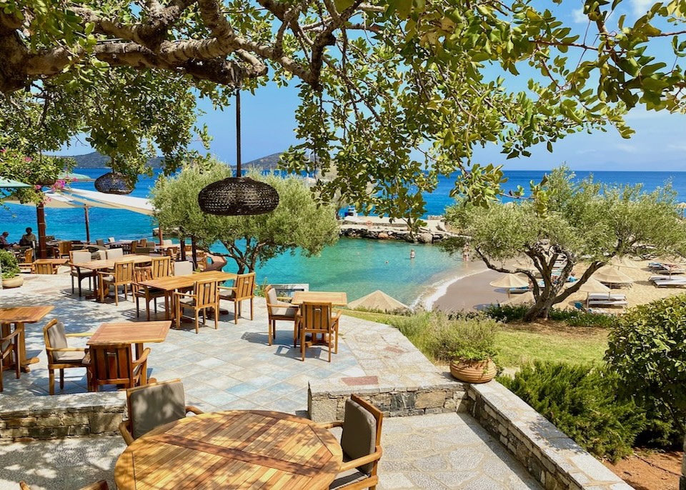 Patio restaurant under a shade tree overlooking the beach at Elounda Mare resort in Crete