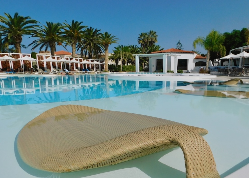 Leaf-shaped rattan sunbeds partially submerged in the shallow side of a pool at Grecotel Caramel hotel in Crete