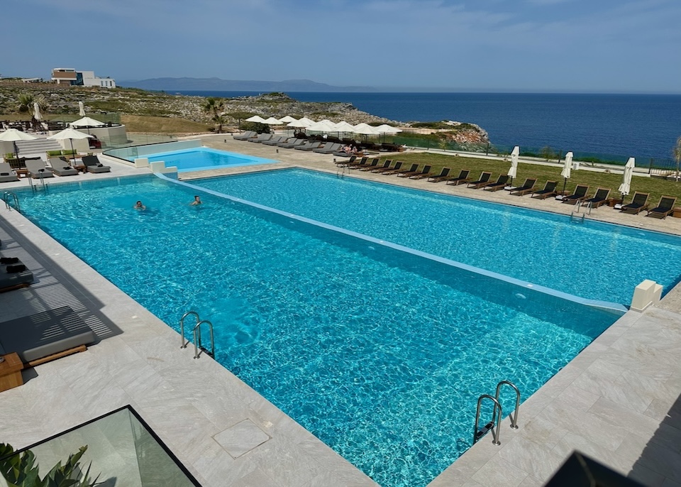 Two seafront pools and a kids pool with a row of sunbeds and green lawn above the sea at Isla Brown resort in Crete