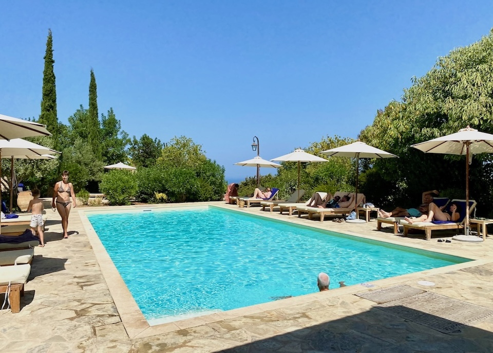 Swimming pool with a stone sun terrace, sunbeds, and greenery at Kapsaliana Village hotel in Crete