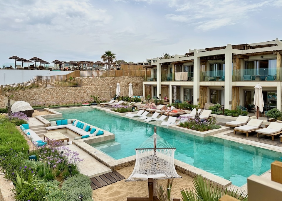 Beachfront pool in front of a a two-story building with a sunbeds and a garden at Mitsis Renela resort in Crete