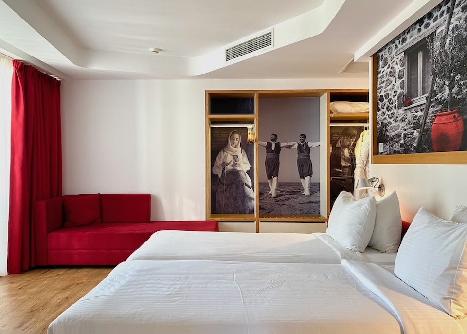 A twin bedded room in white with red accents and black-and-white photography of traditional Greek life at Olive Green Hotel in Crete
