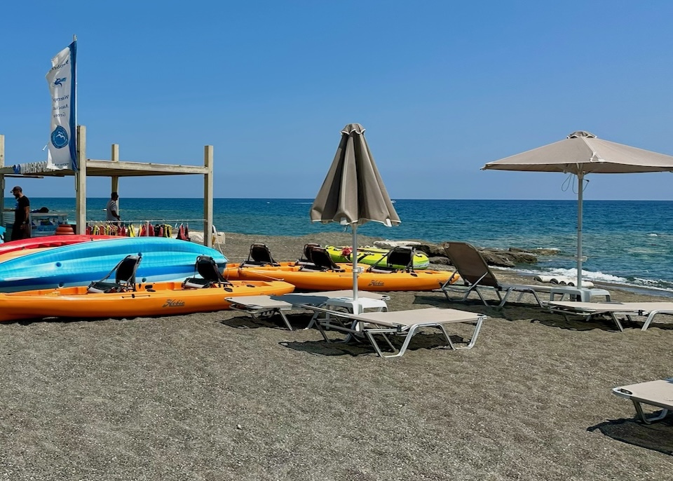 Kayaks, rafts, and sunbeds on a gray sand beach at Ostria Resort in Crete