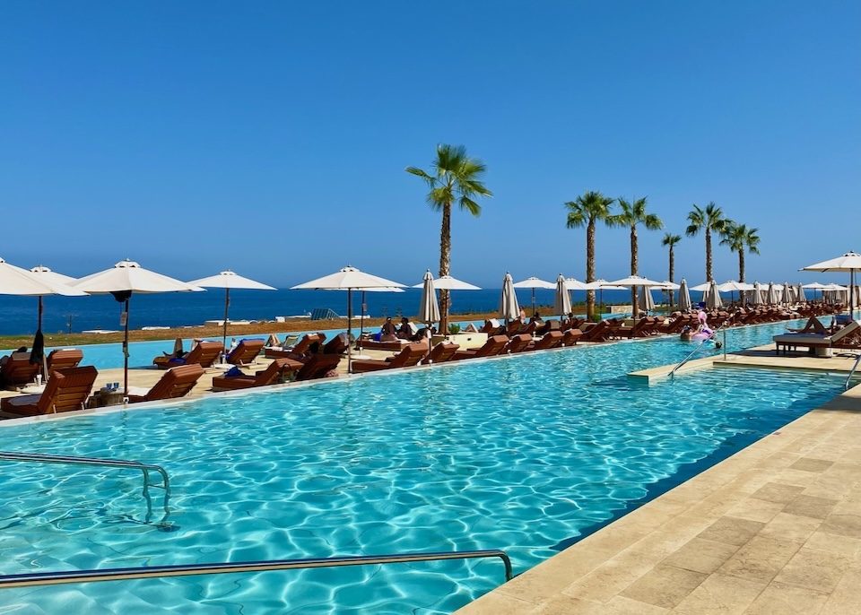 Two long parallel pools facing the sea divided by a row of sunbeds and palm trees at Royal Senses resort in Crete