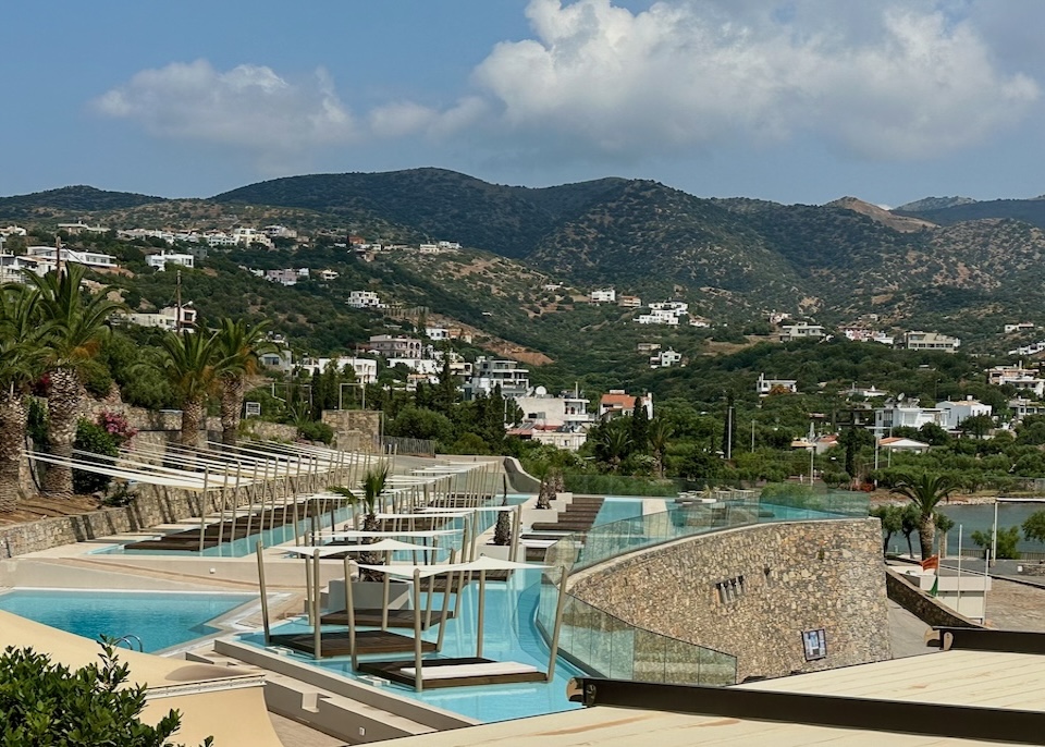 Terraced swimming pools above the sea with green mountains in the background at Wyndham Grand resort in Crete