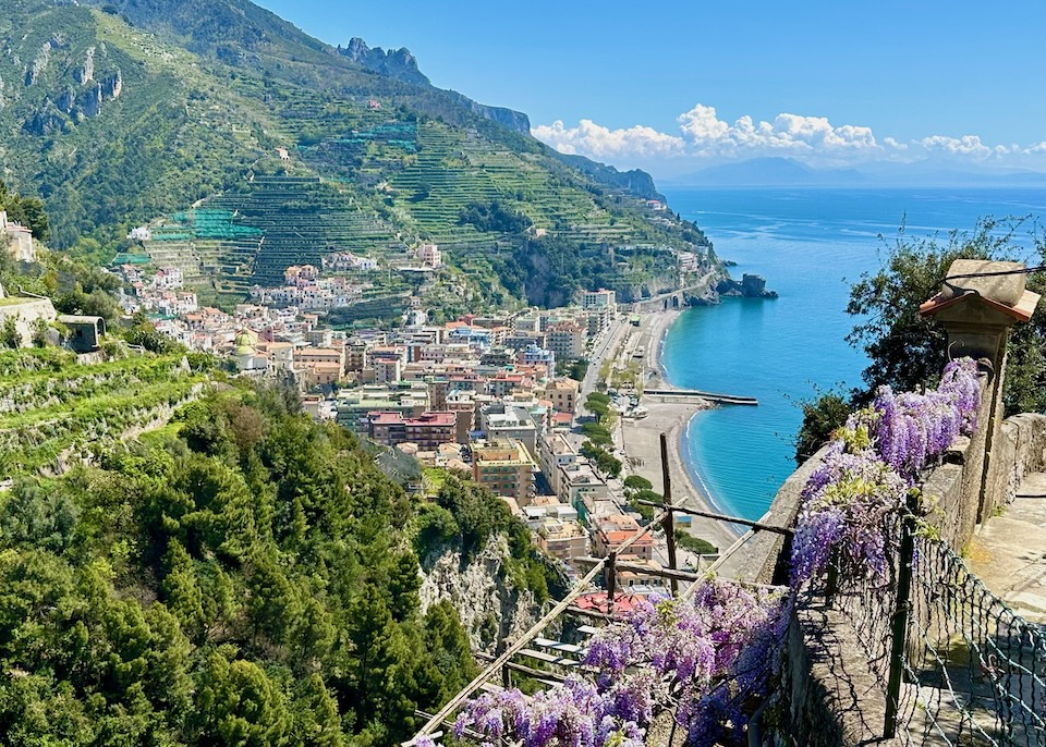View over Maiori town from a wisteria-covered path overlooking the beach, colorful buildings, terraced mountainside lemon groves, and the sea