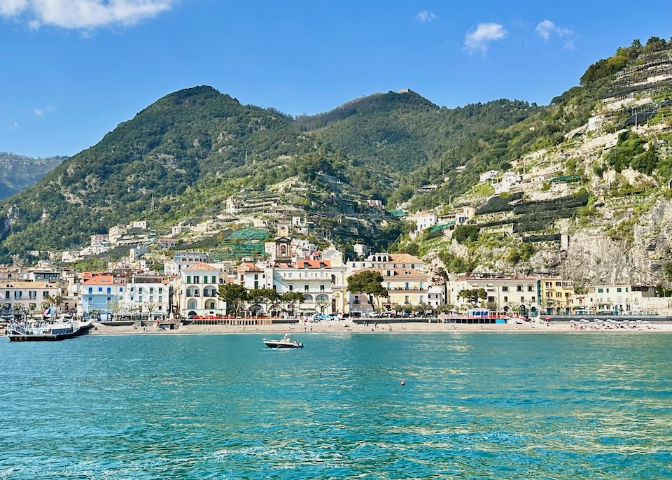 View of the beach and buildings of Minori town with terraced lemon groves carved into the mountains rising behind