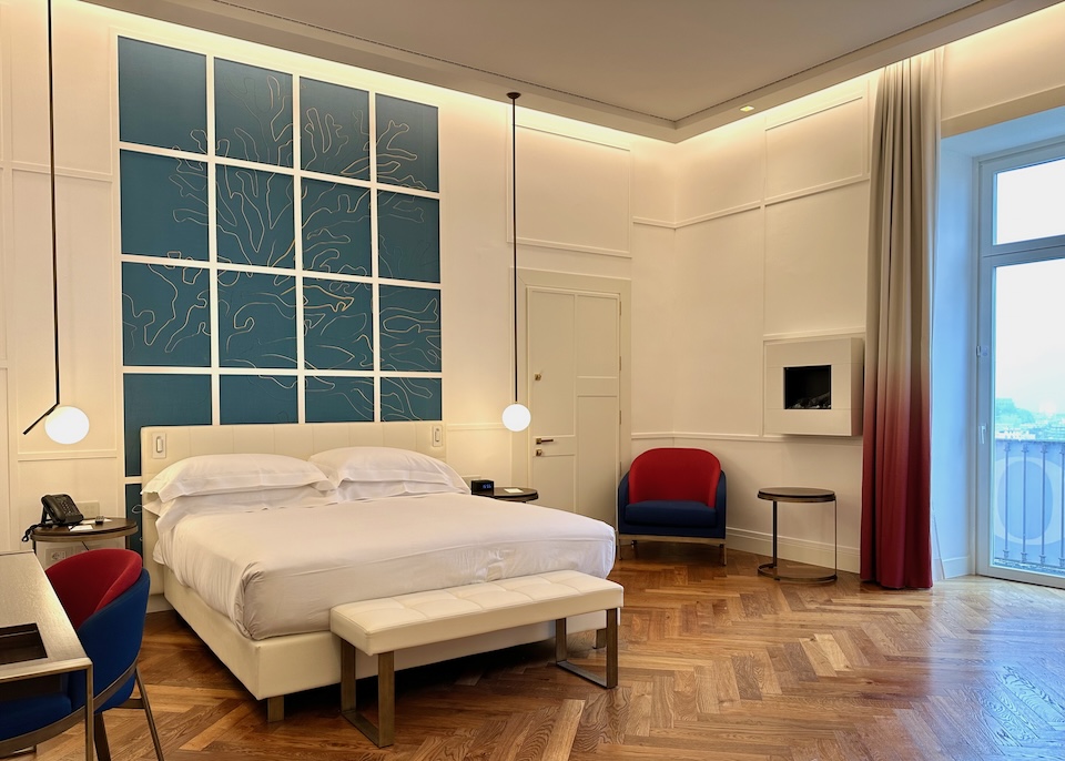 King-sized bed in white with a teal and gold line drawing of a piece of coral and parquet floors in a junior suite at The Britannique hotel in Naples
