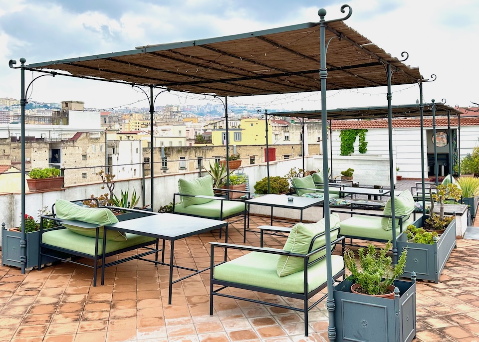 Rooftop terrace with a bamboo pergola, terracotta tile floor, and green cushioned chairs at Santa Chiara hotel in Naples