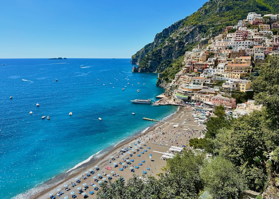 View over Positano's main beach toward the ferry port, colorful hillside houses, and the sea