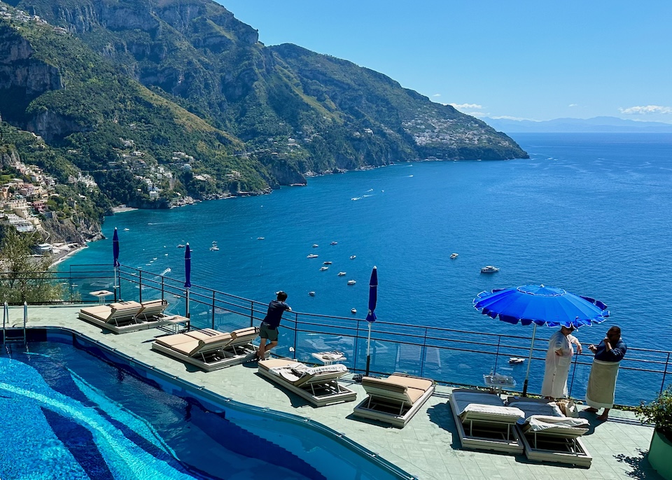Pool with an irregular blue striped pattern and sun terrace overlooking the sea and Positano at Le Agavi hotel