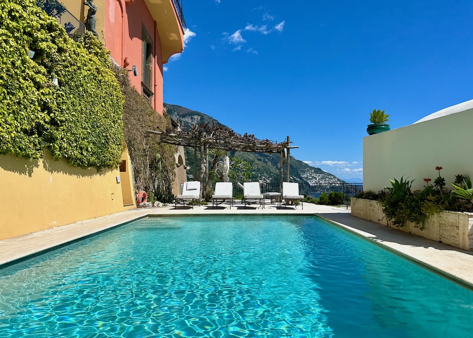 Swimming pool facing a pergola and sunbeds nestled between two buildings at Villa Magia hotel in Positano