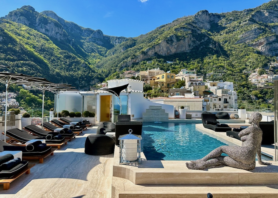 Rooftop pool lined with sunbeds and a sculpture of a woman at Hotel Villa Franca surrounded by mountains in Positano