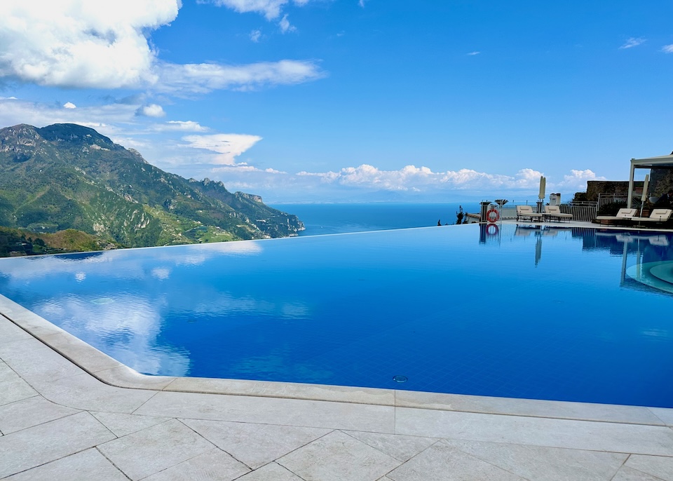 Deep blue infinity pool reflecting the clouds above, facing the sea and green mountains at Caruso hotel in Ravello
