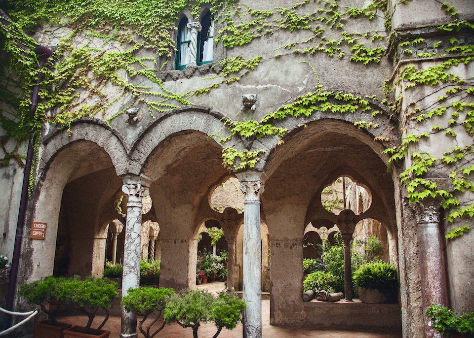 The vine-covered exterior of hte cloister with arches and columns in the garden of Villa Cimbrone hotel in Ravello