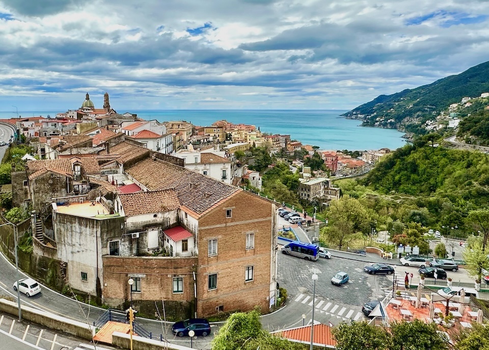 View from the hilltop of Vietri sul Mare with red rooftops on white and brick buildings set along a curvy road and cascading down the green hill to the sea
