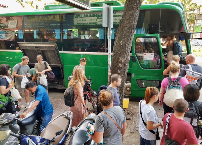 People line up to board a green bus to Cambodia.