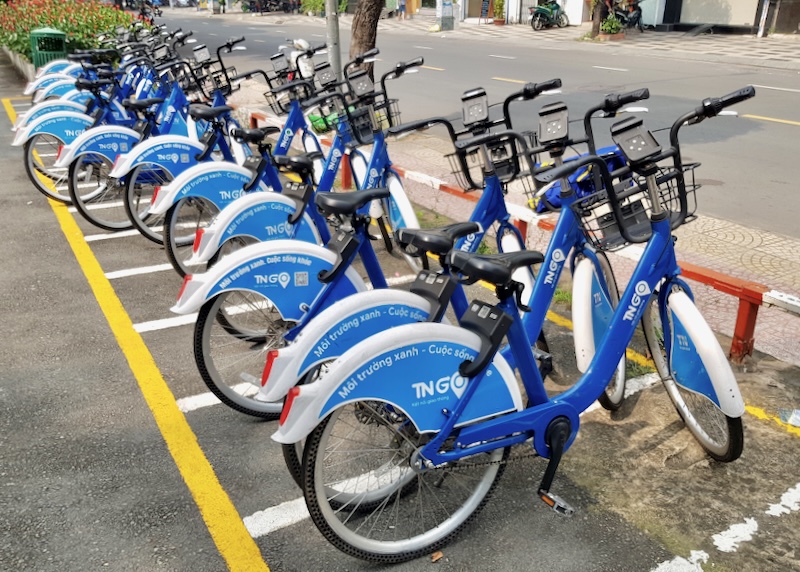 A row of bright blue electric bikes sits along a street.