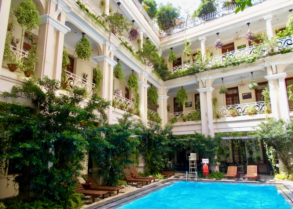 An outdoor pool sits in a courtyard surrounded by balconies overflowing with green plants and flower baskets.