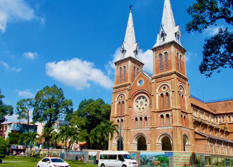 A tall red brick church with twin towers and white pointed roofs.