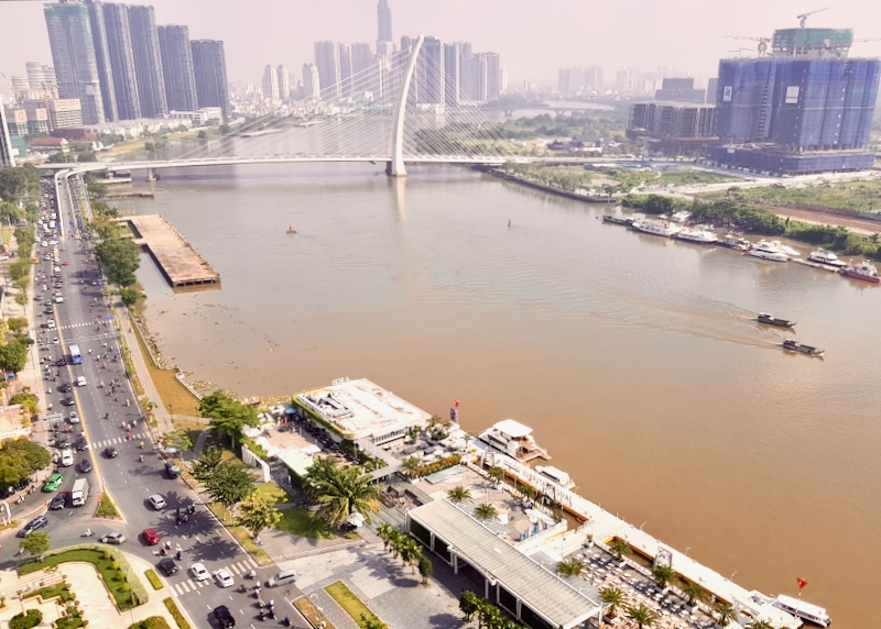 Sky view of the brown Saigon River with a white arched bridge with tension wires.