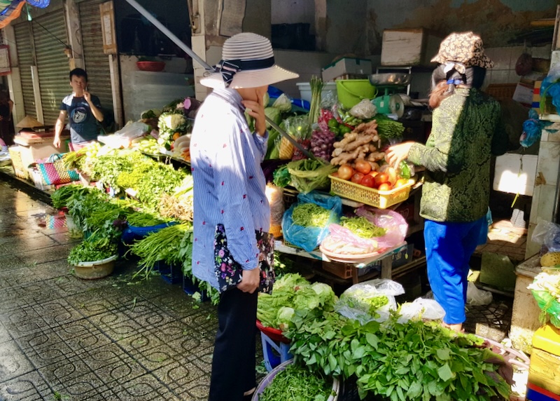 A woman decided between lots of green veggies at an outdoor produce stand.