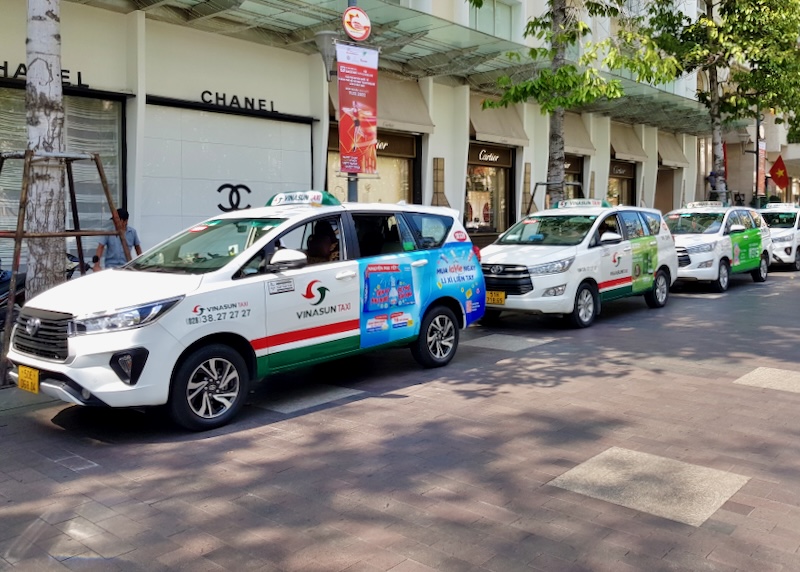 A line of white taxis with the name Vinasun on the doors sit along a curb, waiting for passengers.