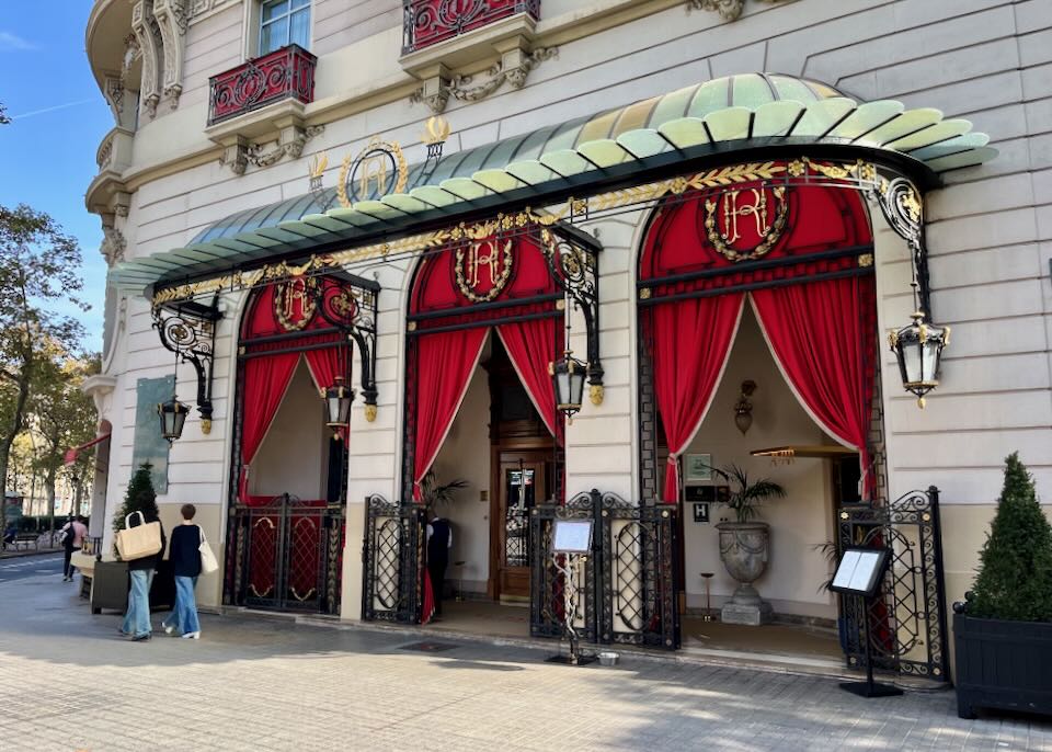 Exterior entrance of an elegant hotel, with red velvet drapery hung in stone archways