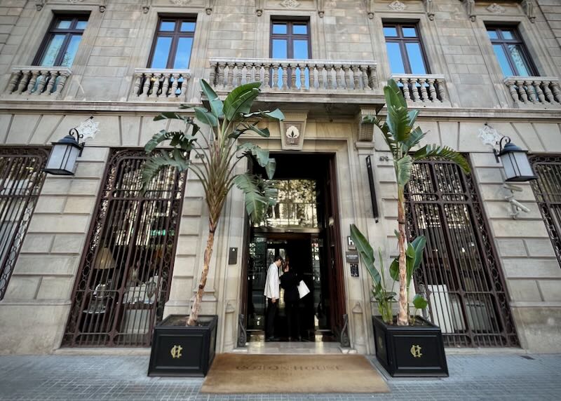 A doorman helps a passerby at a luxury hotel entrance flanked by two palm trees