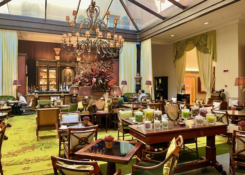 A lavish bar with lush green rugs, brown wood, and rust colored flower arrangements.