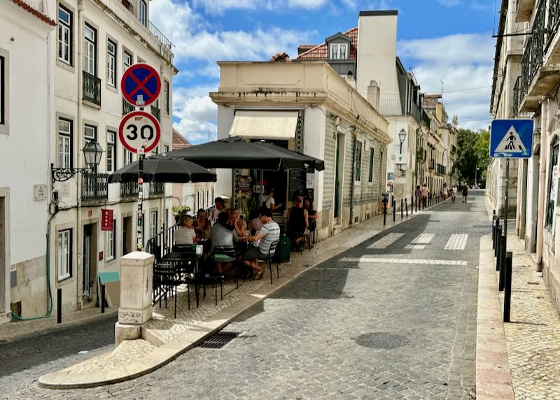 People eat at a cafe perched on a corner of a steep hil in Lisbon