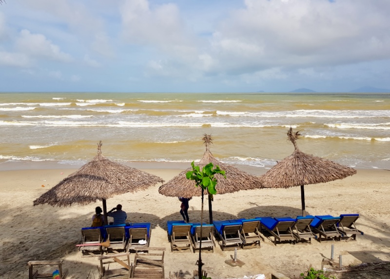 A couple sits in lounge chairs on the sand by the ocean.