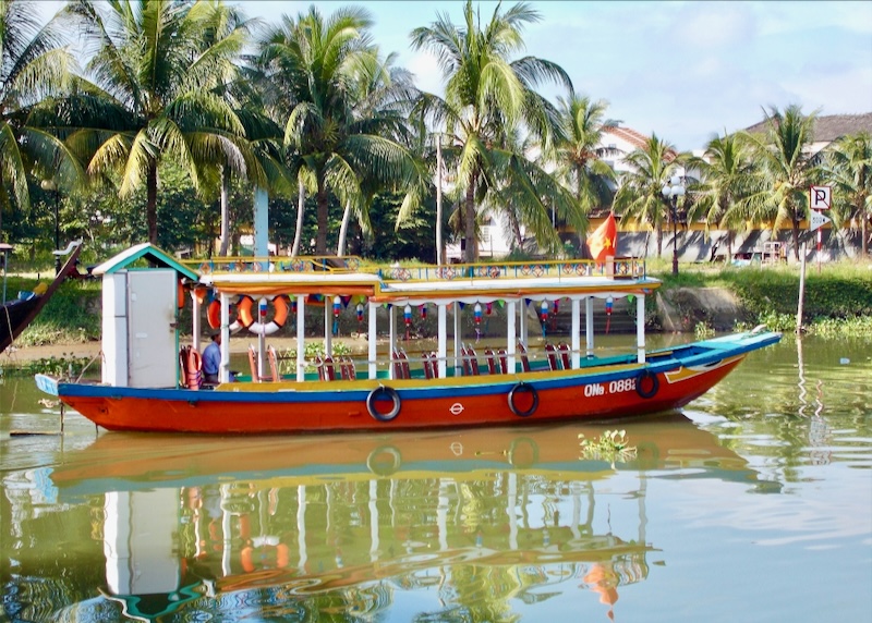 A red, white, blue, and yellow boat rides along the light green river waters.