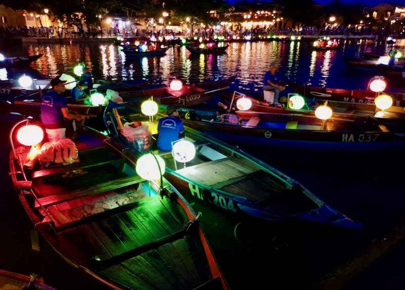 Small boats lit with lanterns at night sit waiting for guests to ride.