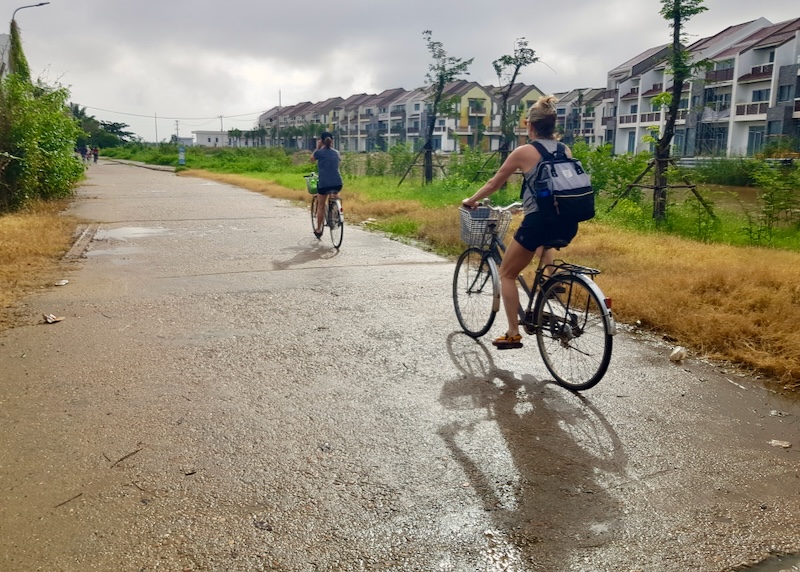 Two women ride bikes on a wide sidewalk.