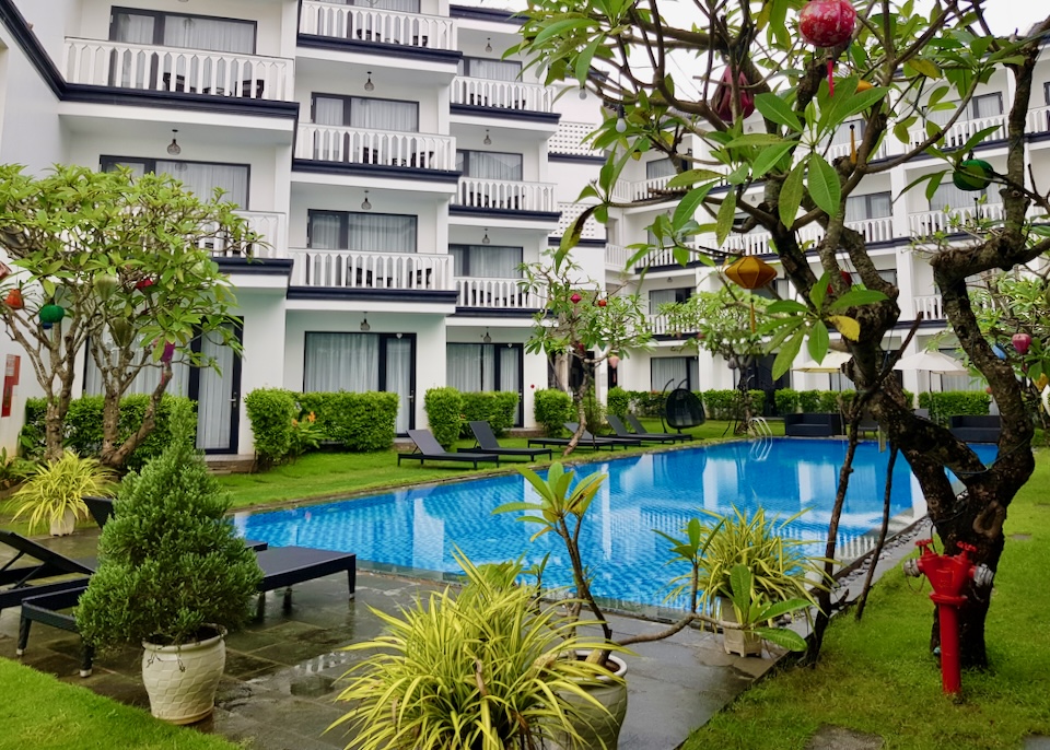 A bright blue pool sits next to tall hotel room balconies.